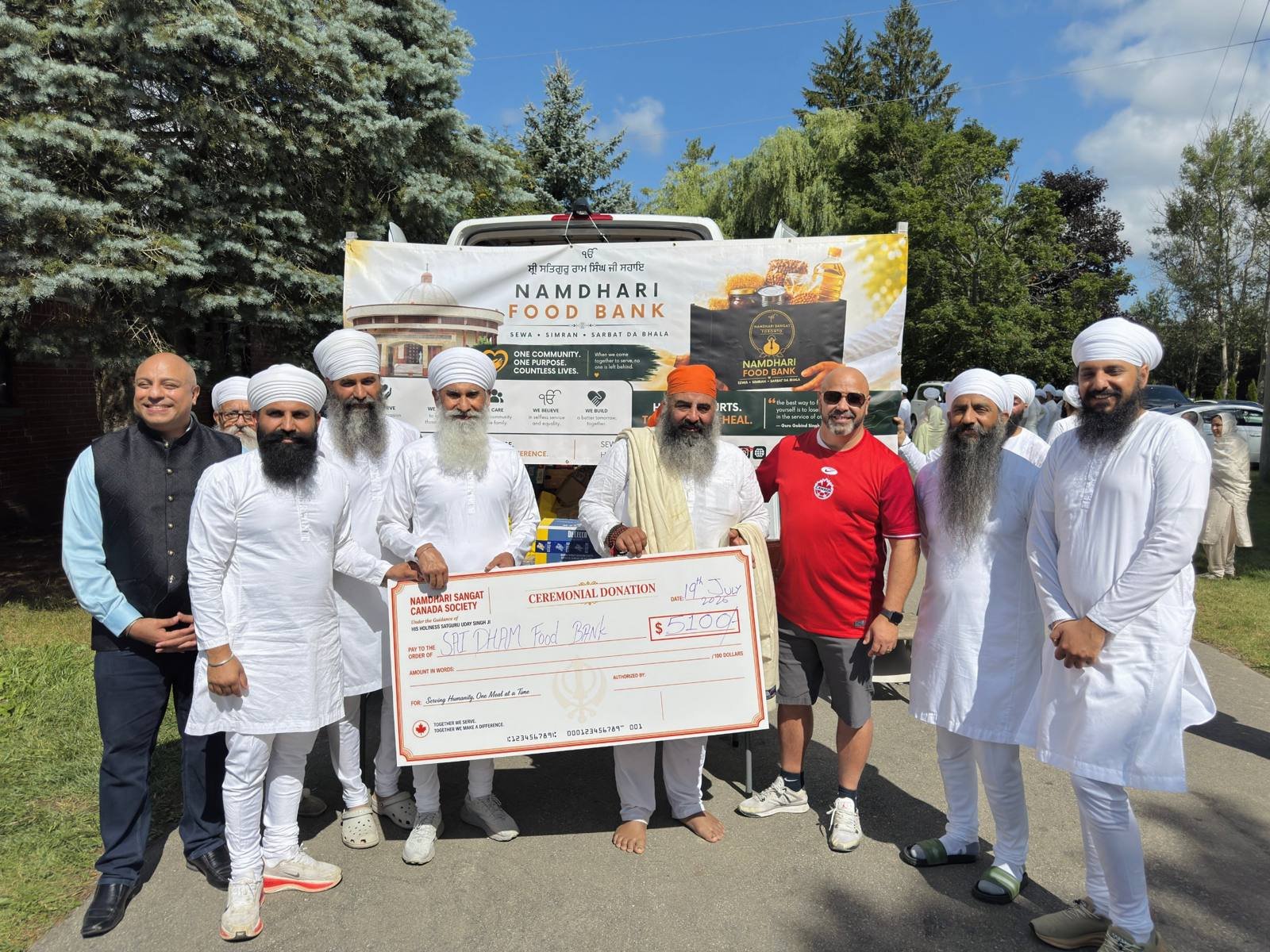 Sevadars presenting a ceremonial cheque to Sai Dham Food Bank in front of the Namdhari Food Bank banner